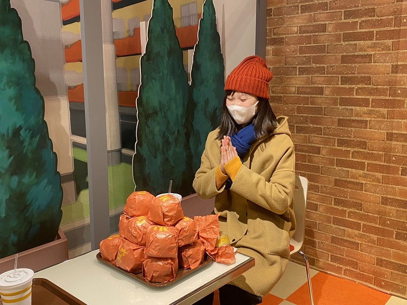 A CET Japan student sitting in a prayer position in front of large wrapped burgers in TOEI Kyoto Studio Park
