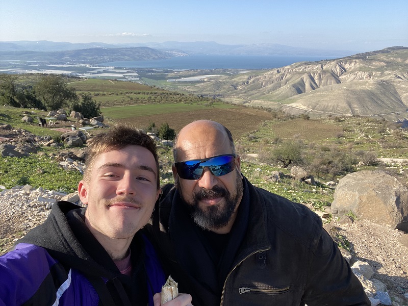 A CET Jordan student smiling with his Uber driver with a scenic view of mountains and a large body of water behind them