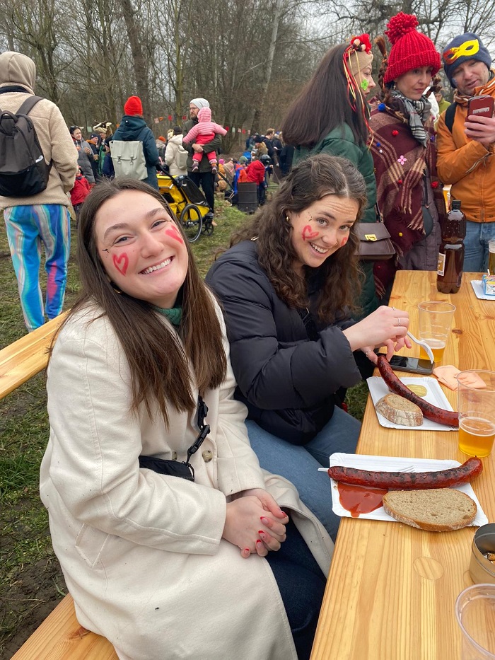 Two CET Prague students with red hearts drawn on their faces as they smile at a table with sausage, bread, and beer