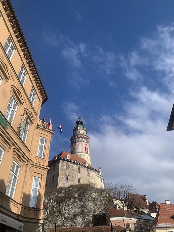 A view of the green and faded red tower in Český Krumlov with a yellow building to the left and other buildings below