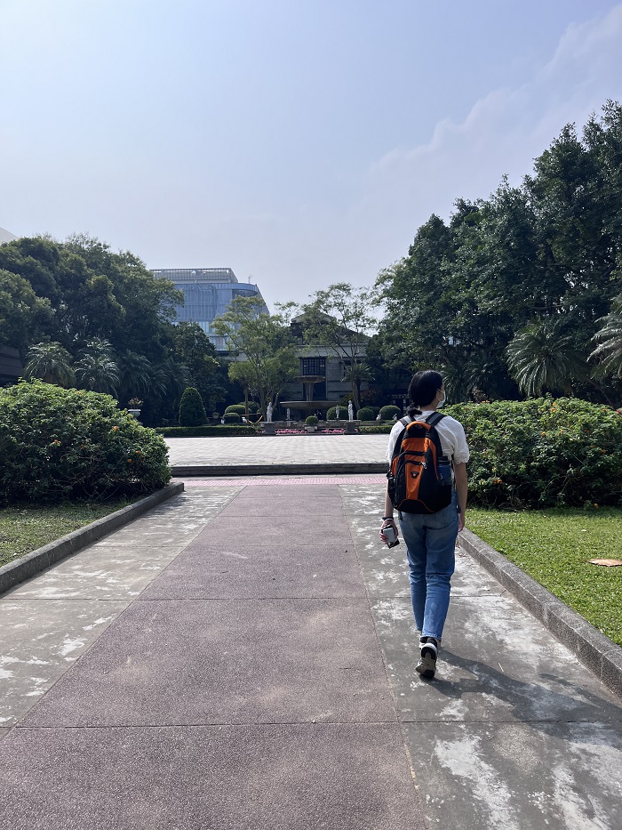 A person with a backpack walking the grounds of the Songshan Cultural Park, surrounded by greenery 