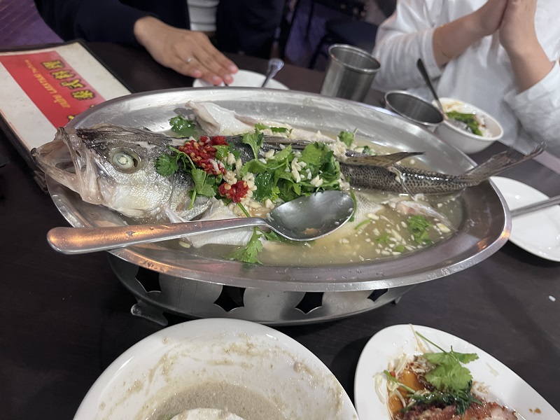 A cooked fish with green herbs and spices on top of it in an oval-shaped grey bowl