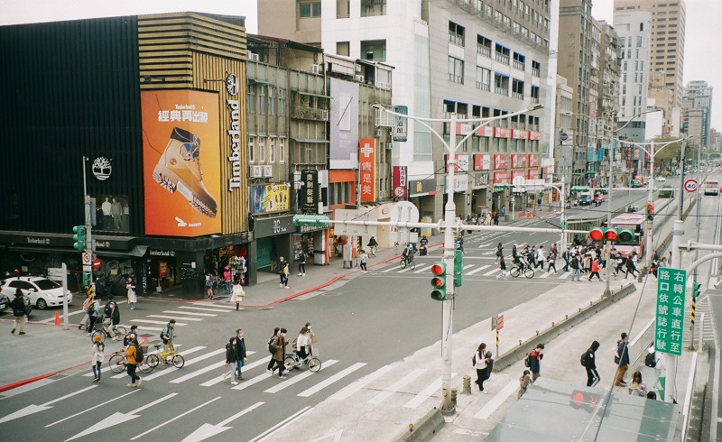 A view of the Gongguan area in Taiwan with people walking across streets, Timberland clothing store, pharmacy, and more