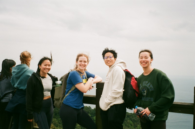 Four CET Taiwan students smiling and leaning against the observation deck that looks over the Pacific Ocean and Turtle Island