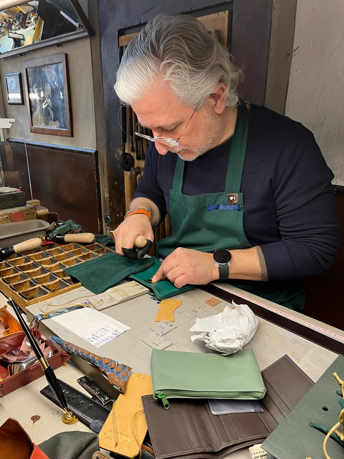 A man engraving initials onto a leather pouch at a store called Scuola del Cuoio in Florence, Italy