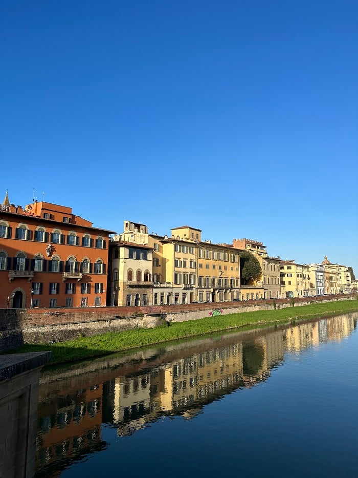 Buildings along the Arno River and the reflection of those buildings in the water on a cloudless day in Florence
