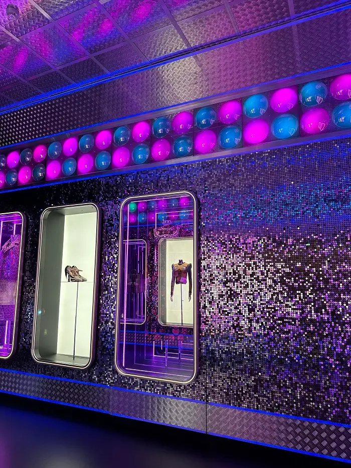 Gucci Garden exhibit with neon purple and blue lights and sparkly walls. There are shoes and clothing pieces on display.