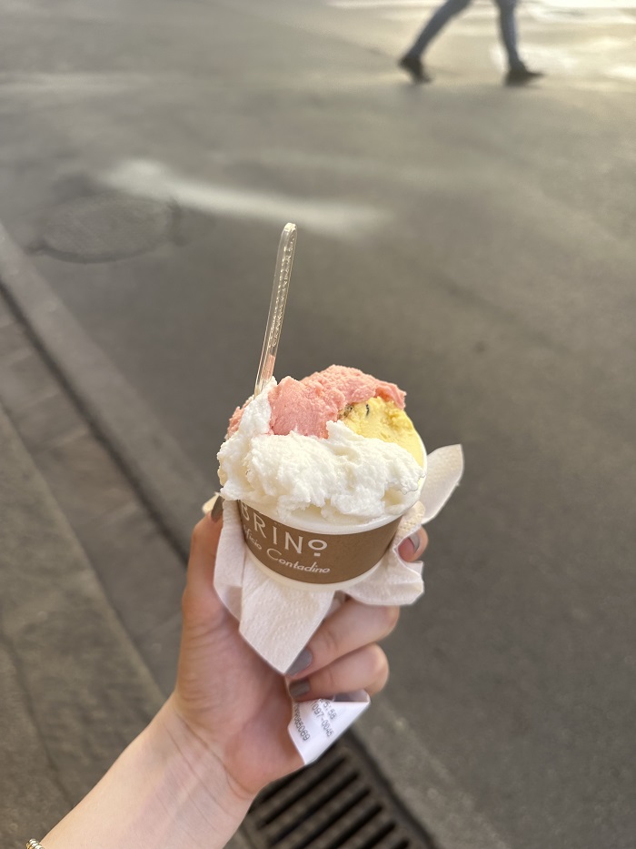 A cup of gelato with three different flavors and a spoon sticking out 