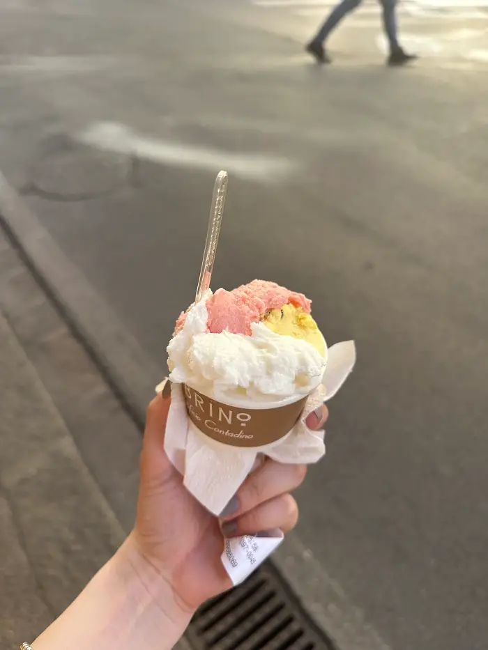 A cup of gelato with three different flavors and a spoon sticking out