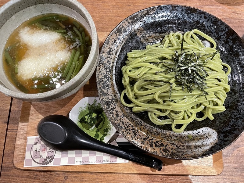 A small bowl of udon soup on the left and a bowl of Matcha noodles on the right, all placed on a small tray