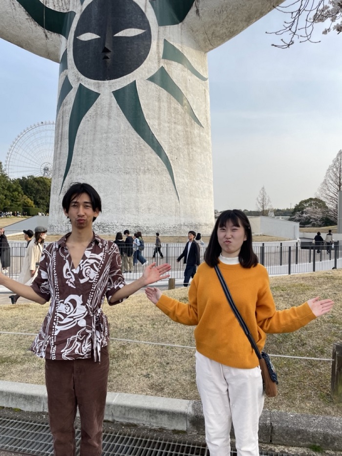 A male and female standing in front of the Tower of the Sun imitating the same exact pose as the Tower of the Sun