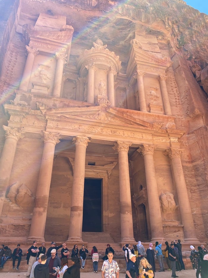 The outside of Petra in Jordan with many people looking at the building and sitting in front of the monument