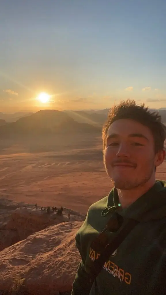 CET Jordan student smiling and taking a selfie in Wadi Rum, Jordan with the sun shining and desert landscape in the back 