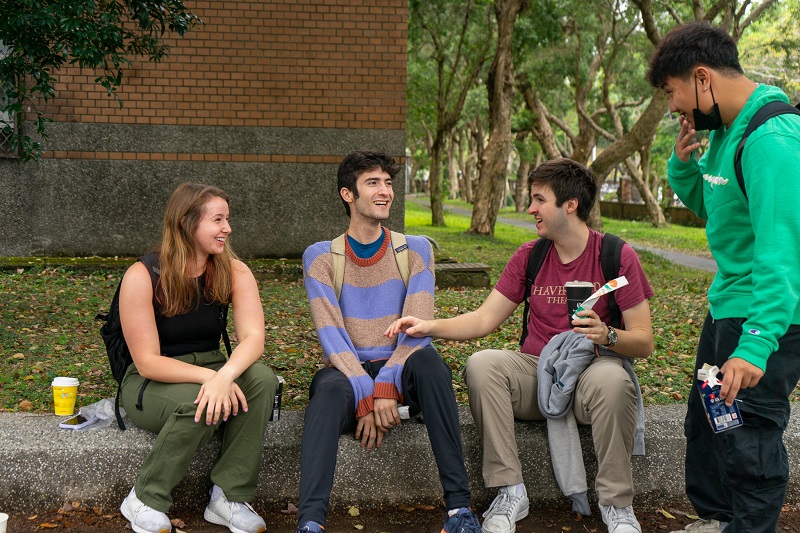 Four CET Taiwan students sitting on a curb in front of a building on National Taiwan university's campus