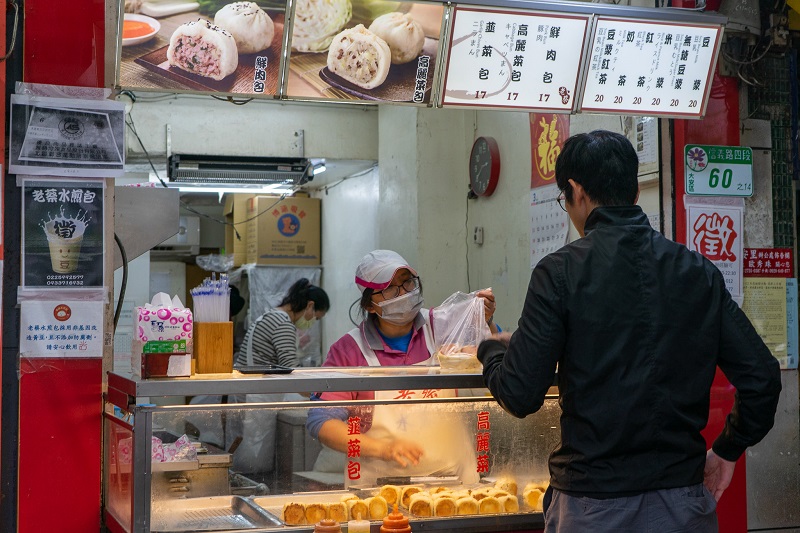 A woman handing over a bag of fried pork buns to a customer