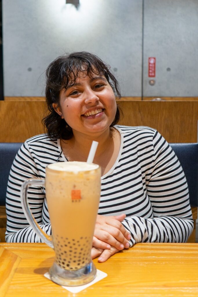 CET Taiwan roommate sitting in a booth  and smiling in front of a large Boba drink with a straw