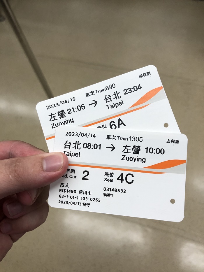 A hand holding up two train tickets for trips between Taipei and Zuoying