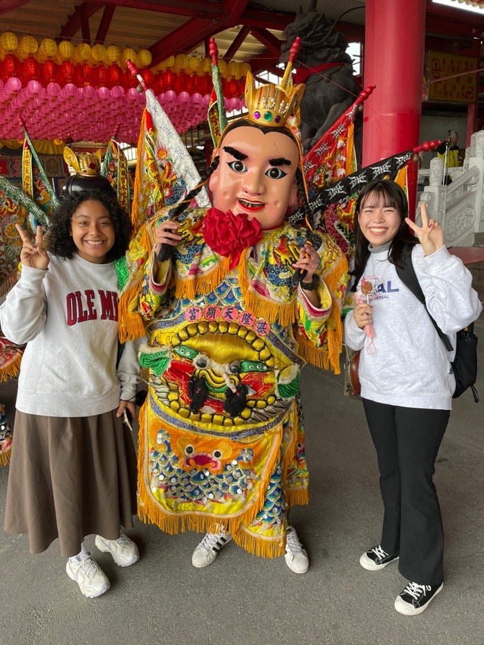 A CET Taiwan student and her friend standing at the sides of a person in a ritual costume at Tianxian Temple