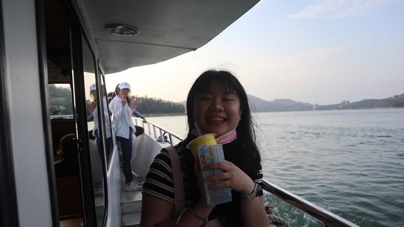 A CET Taiwan language partner smiling while holding a ticket and drink in one hand on a boat