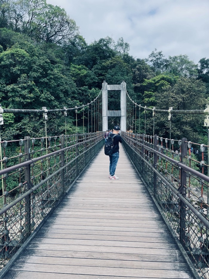 Someone with a backpack standing and facing away in the middle of a bridge in Shifen District