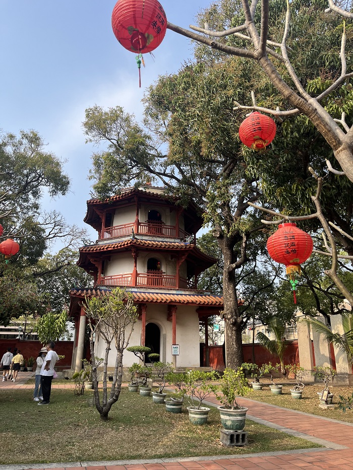A small three-story building that looks like a temple in the midst of trees with red lanterns hanging from branches in Taiwan