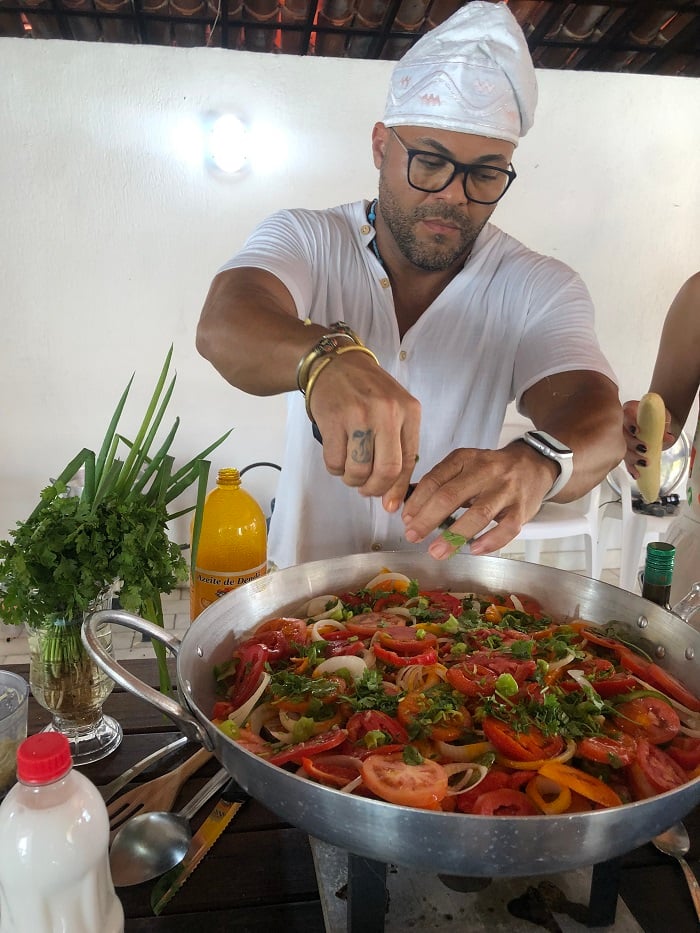 A cooking workshop instructor making moqueca in a large steel pan