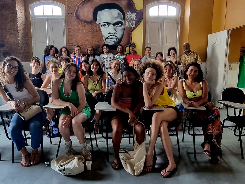 Group of CET Brazil students sitting at desks and standing along a mural of Steve Biko at the Steve Biko Institute in Brazil