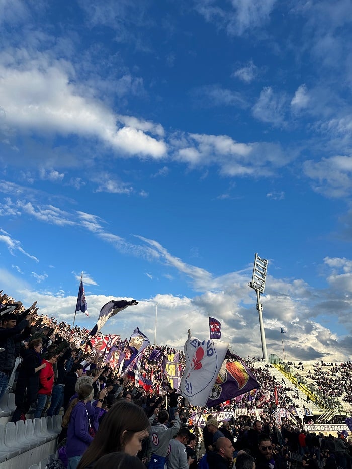 Fans standing and waving flags at the outdoor Fiorentina soccer game