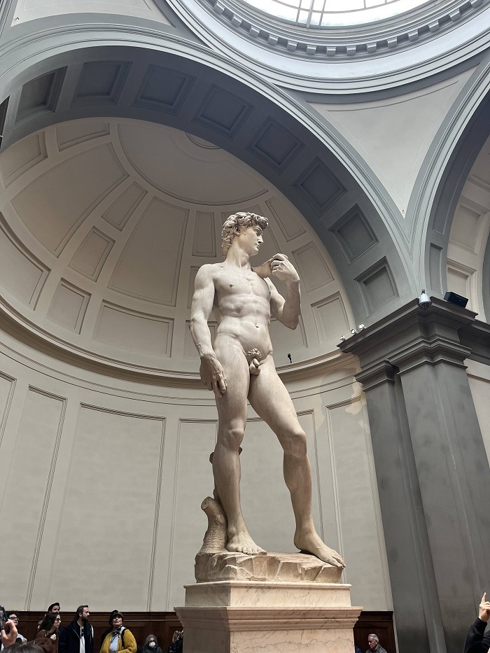 The David statue in the Accademia Gallery with people surrounding the base of the artwork in Florence