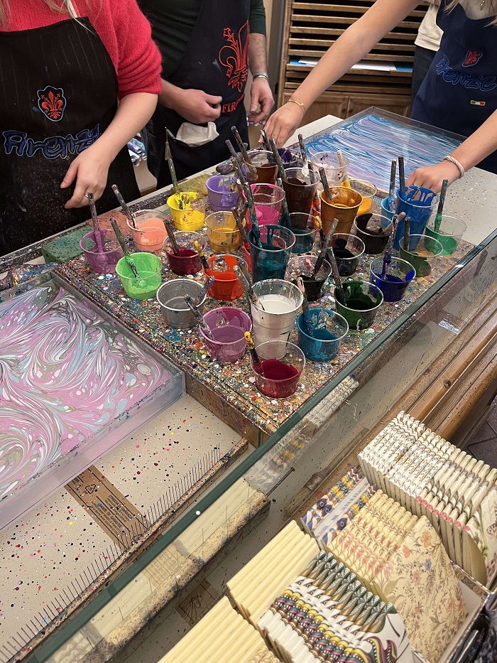 Many small cups filled with paint on a table with hands marbling paper