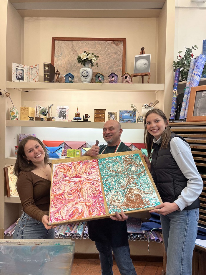 Two CET Florence students and a male holding up their marbled paper artwork together inside of an art shop