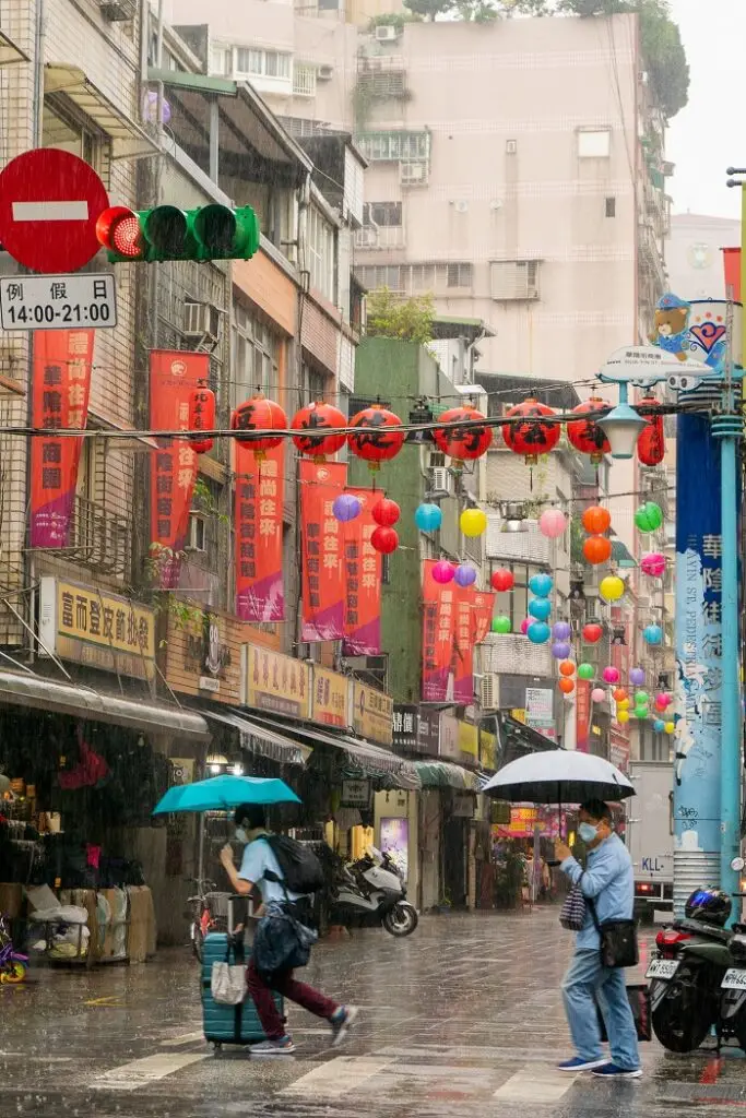 Locals in Taiwan holding umbrellas while walking across a small street in the rain