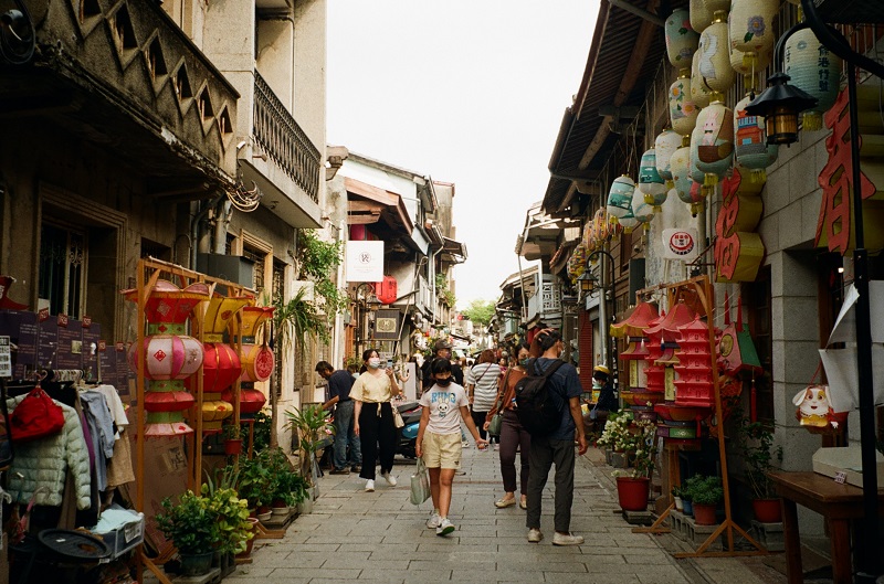 Shennong street full of little side shops, lanterns adorning the sides of the street, and people observing shops while walking in the middle of the path