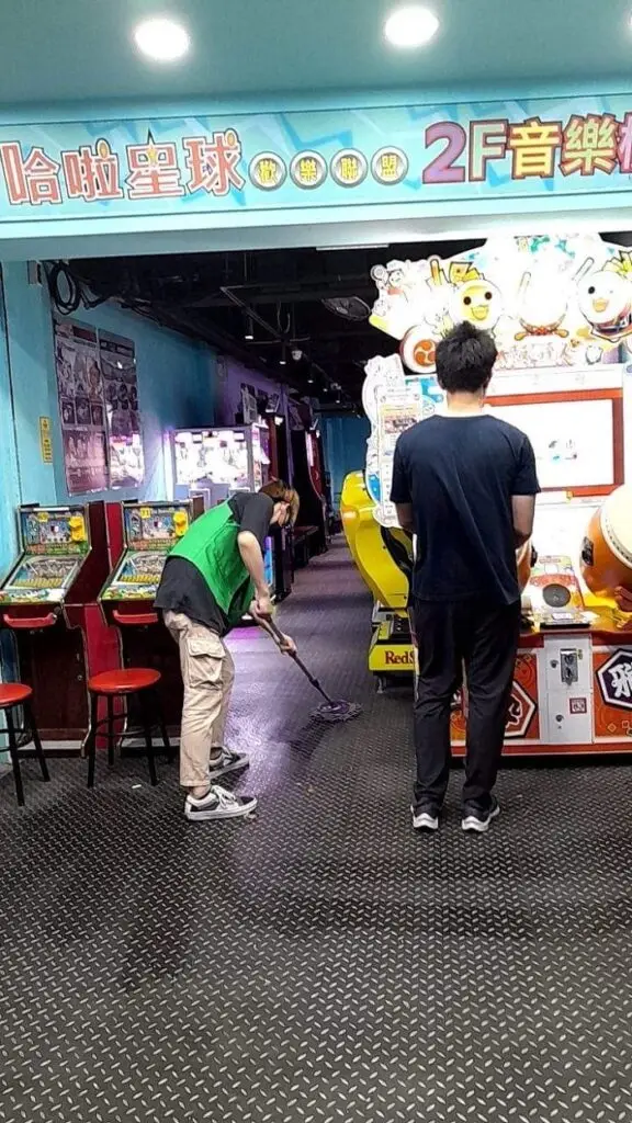 A person playing a game inside an arcade called Hala Planet in Taiwan next to an employee mopping the floor