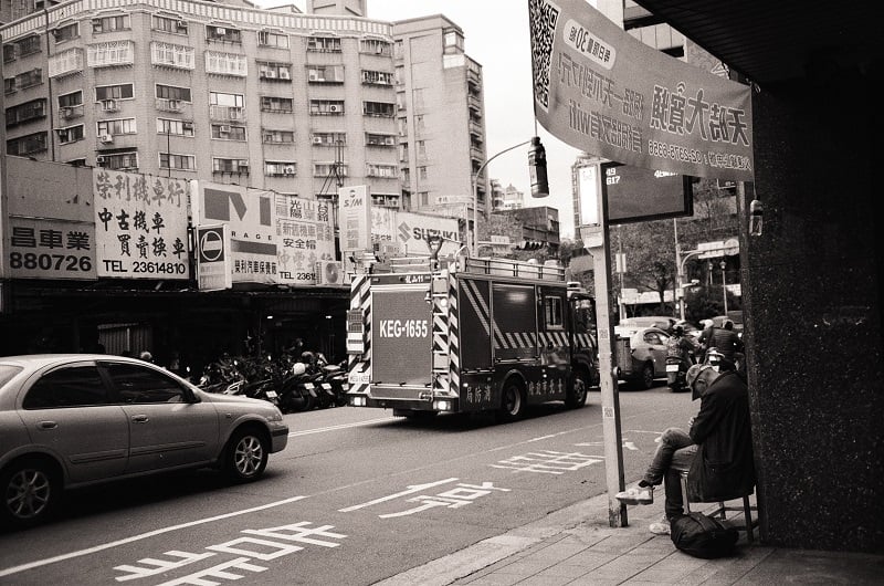 A street with cars and a truck in Taiwan with a person waiting with his head down at a bus stop