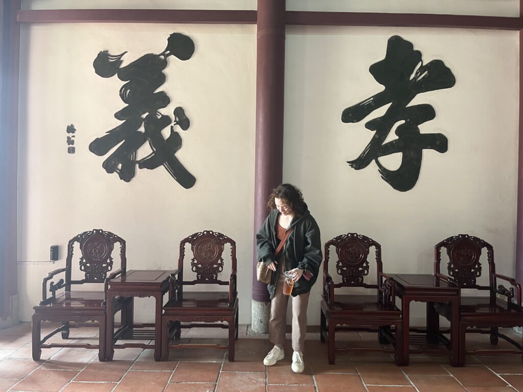 Someone standing in front of a wall of calligraphy that says “Filial Piety” or “Devotion to one’s parents and loyalty to friends"