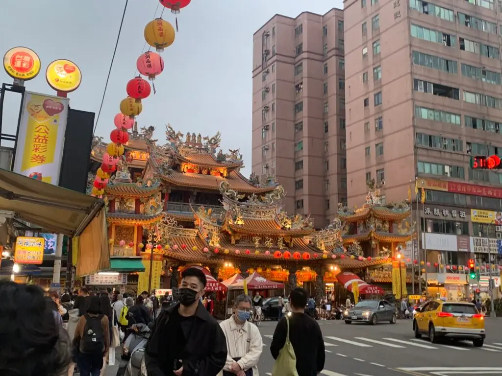 People on the sidewalks and cars in the steet by the entrance of Raohe Market after exiting Songshan station in Taiwan