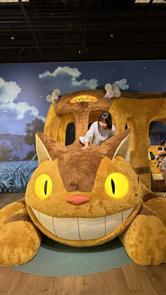 A female AICAD in Japan student looking down at the Neko bus within Ghibli Park