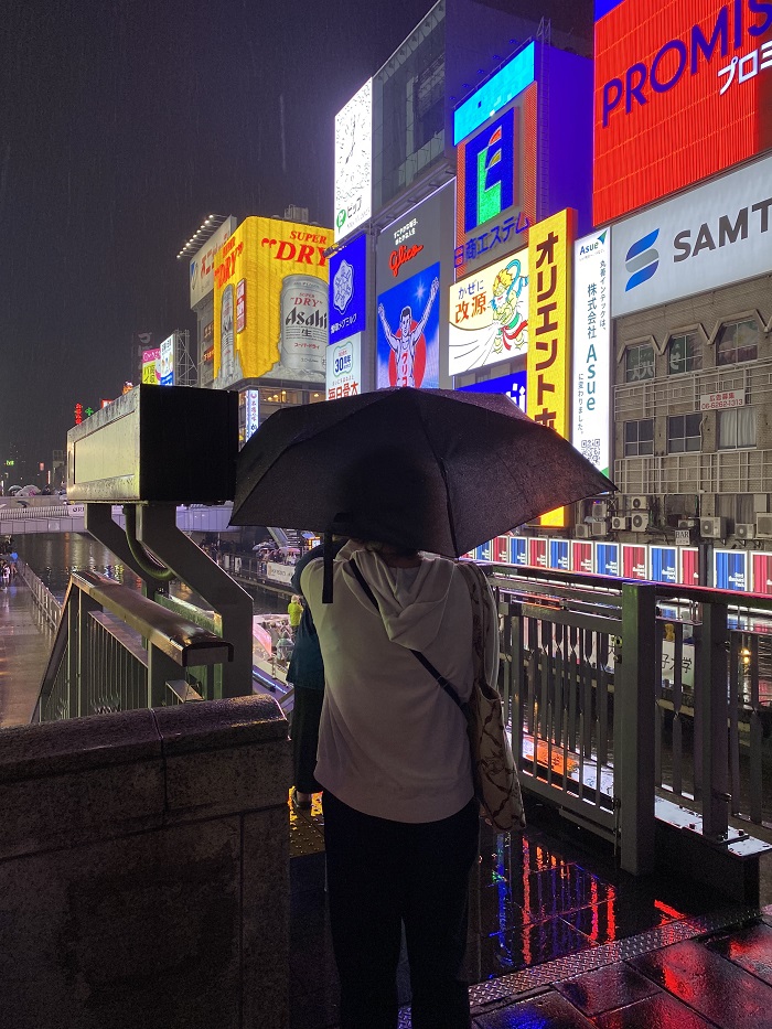 Someone taking a photo of the neon billboards while under an umbrella in Dotonbori, Japan