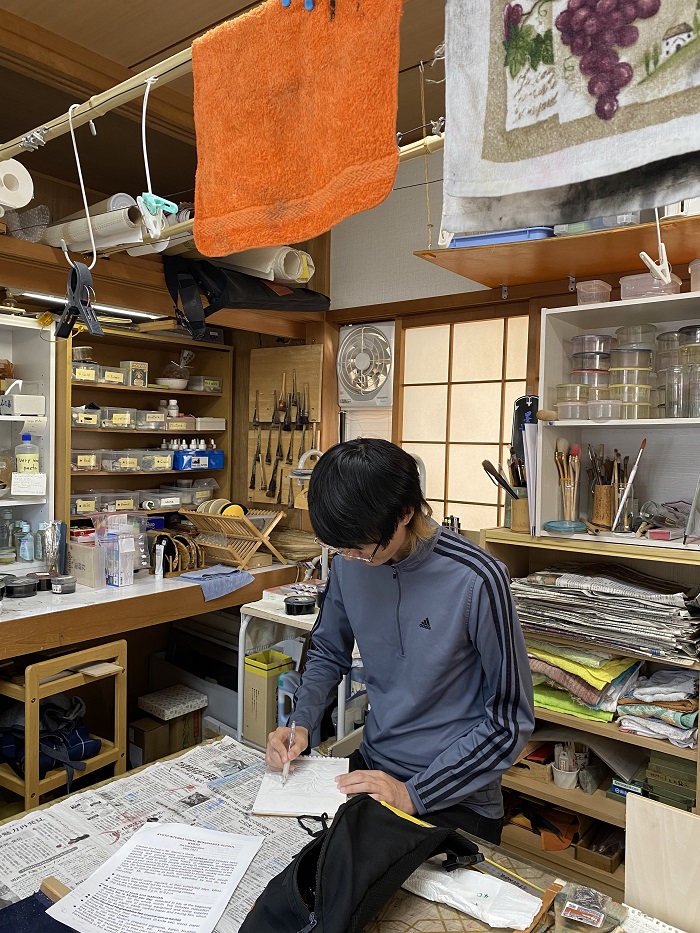 A male AICAD in Japan student sketching in a cluttered woodblock printing studio in Japan
