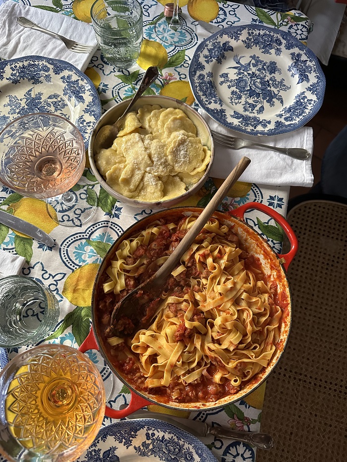 A kitchen table set with fresh pasta in bowls, wine, and forks.