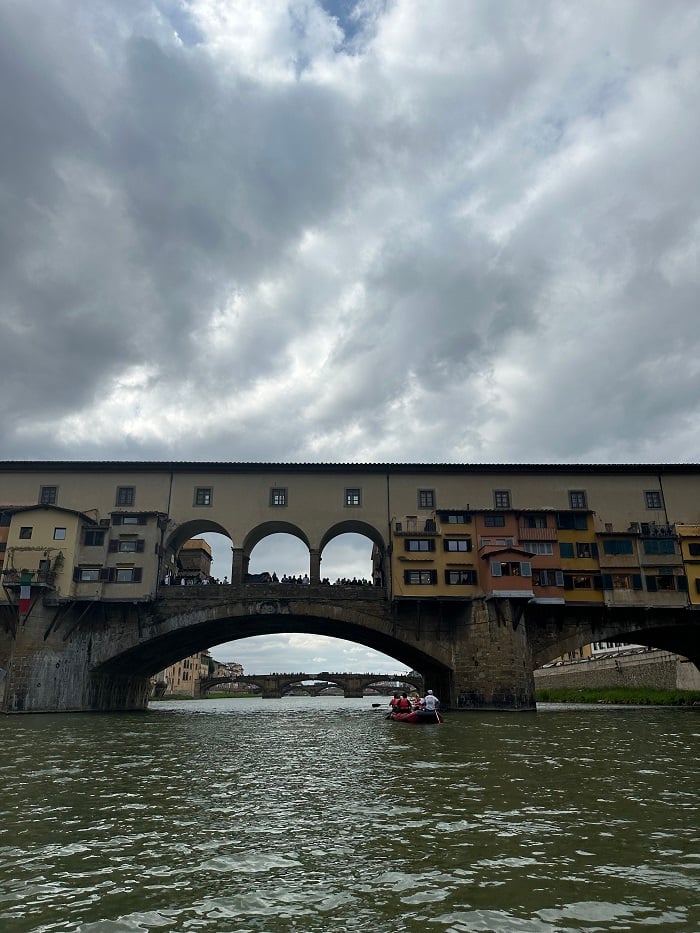 A small boat rafting away, towards Ponte Vecchio on the Arno River in Florence on a cloudy day