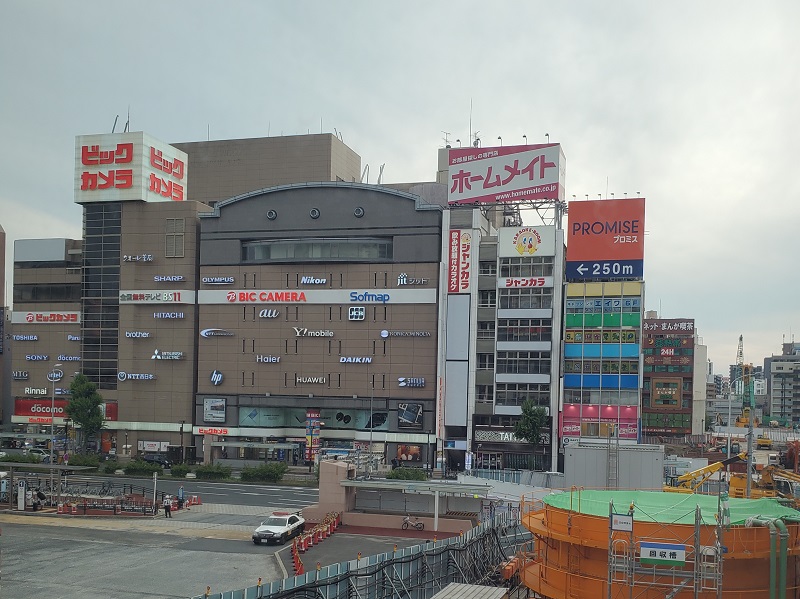 A large building with many different shops such as HP, Daikin, and Nikon and some construction on the side of the building in Japan