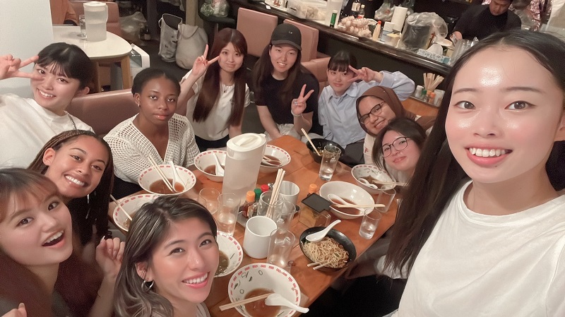 A large girl group of CET Japan students smiling with empty ramen bowls on the table in a restaurant in Japan