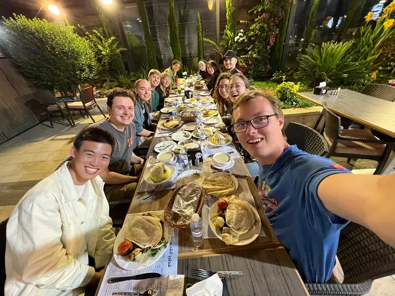 A large group of CET Jordan students sitting outside around a long rectangular table with authentic Middle Eastern food on plates in front of each person