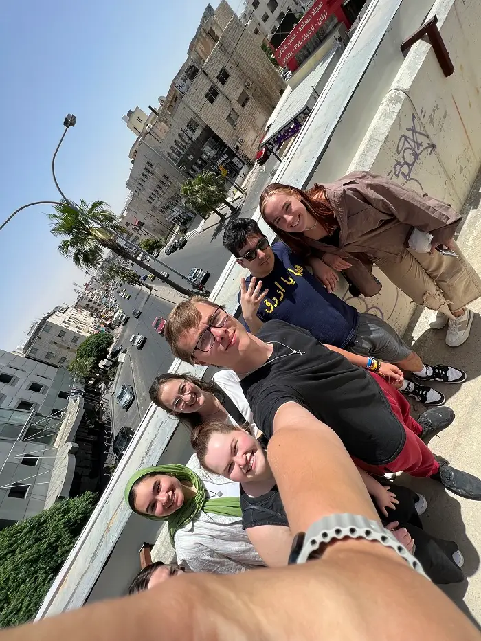 Seven CET Jordan students smiling on a pedestrian bridge above a street with cars in Jordan