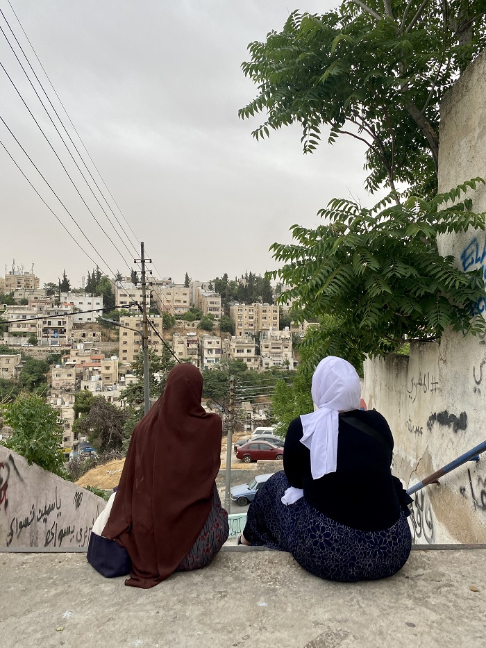Two people sitting on the top of a staircase outdoors, looking towards the cityscape view of Amman, Jordan