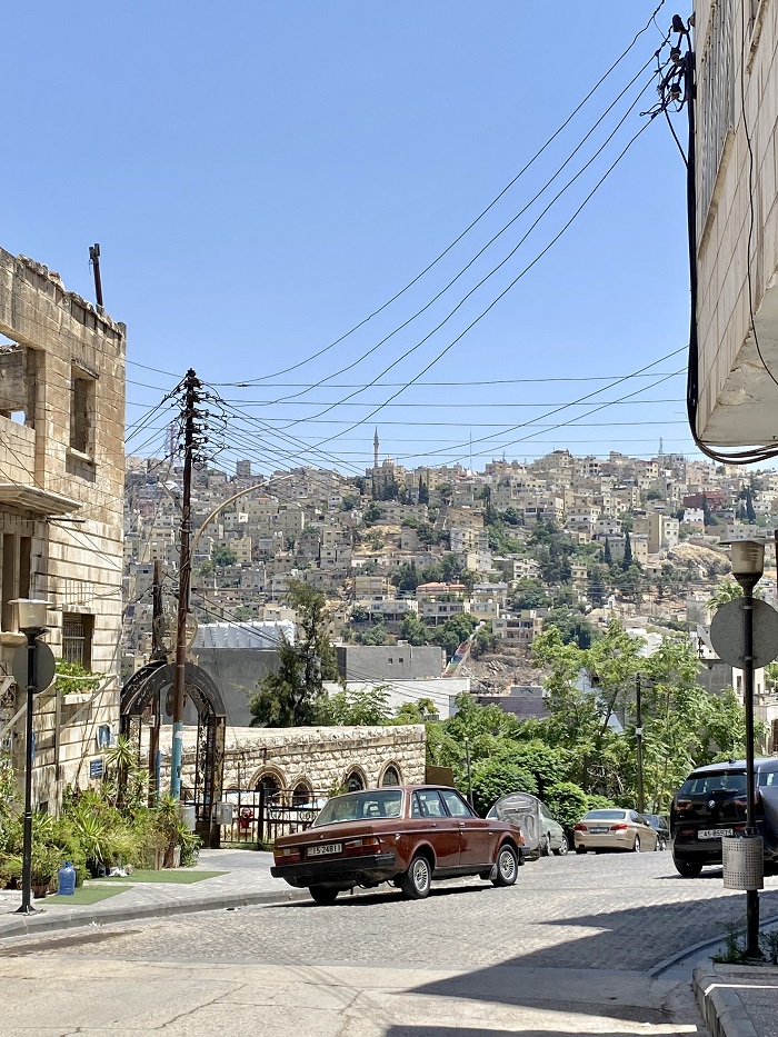A street scene of Amman, Jordan with a few parked cards and layers of houses afar