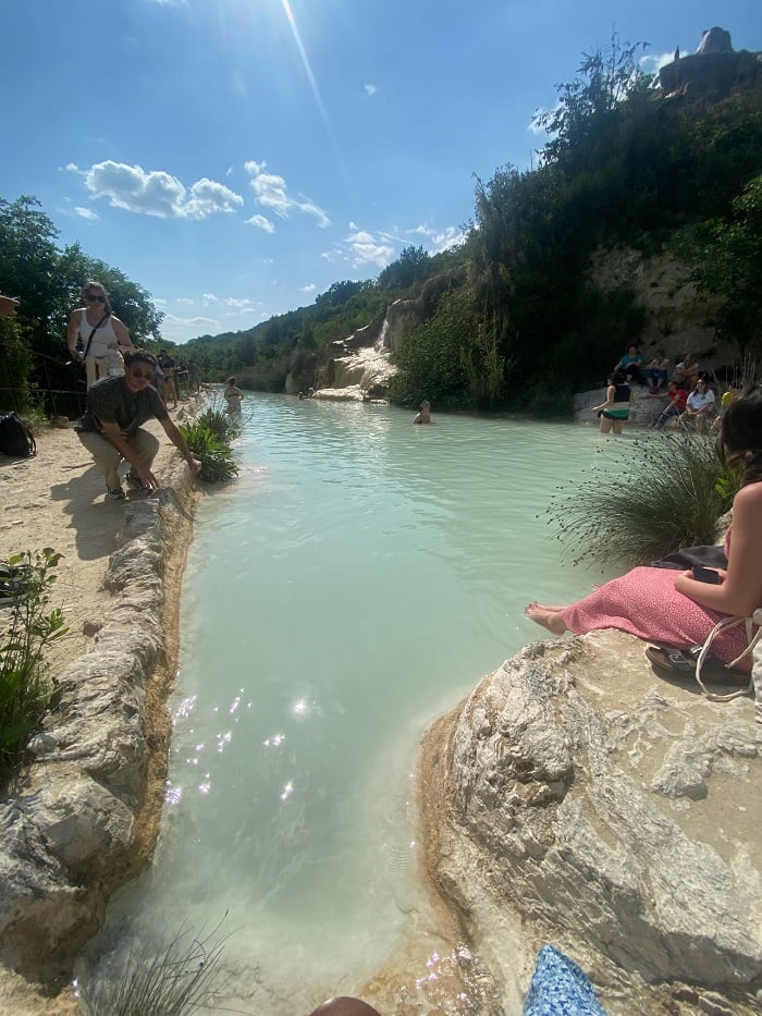 A few people soaking their feet in the natural spring pools near the base of the Bagno Vignoni mountain in Italy