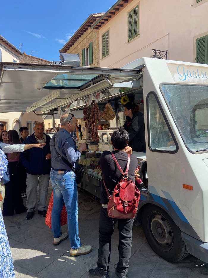 People standing outside of a truck that sells meats and cheese in Siena, Italy